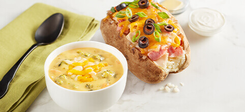 McAlister's Choose 2 combo, featuring a loaded baked potato with meats and cheeses, paired with a side of brocoli cheddar soup in a small white bowl. 