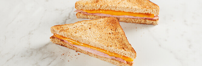 A sliced ham and cheese melt sandwich on toasted wheat bread.