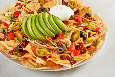 Ultimate nachos topped with melted cheese, sour cream, avovado slices, salsa, and jalapeños.