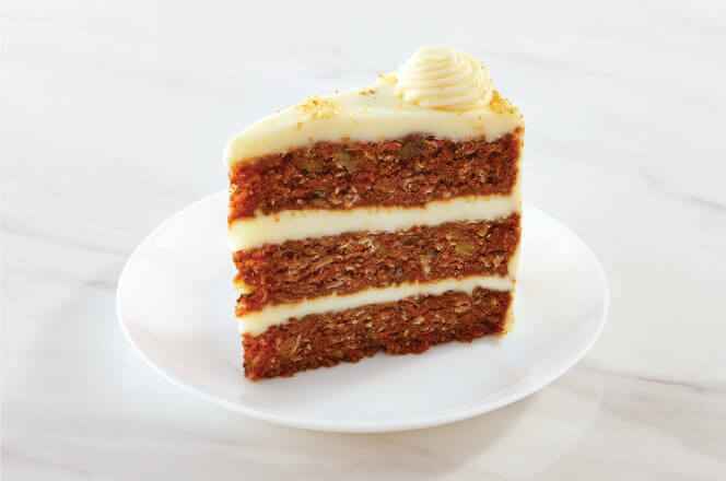 A slice of colossal carrot cake with layers of cream cheese frosting and walnuts baked inside.