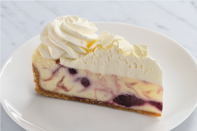 A slice of berries and cream cheesecake, topped with whipped cream and icing.