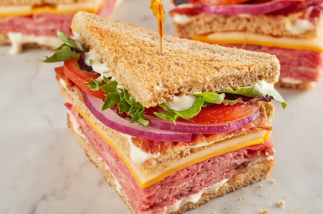 A Black Angus Club sandwich with roast beef, bacon, cheddar, Swiss, lettuce, tomato, and horseradish sauce on wheat bread.