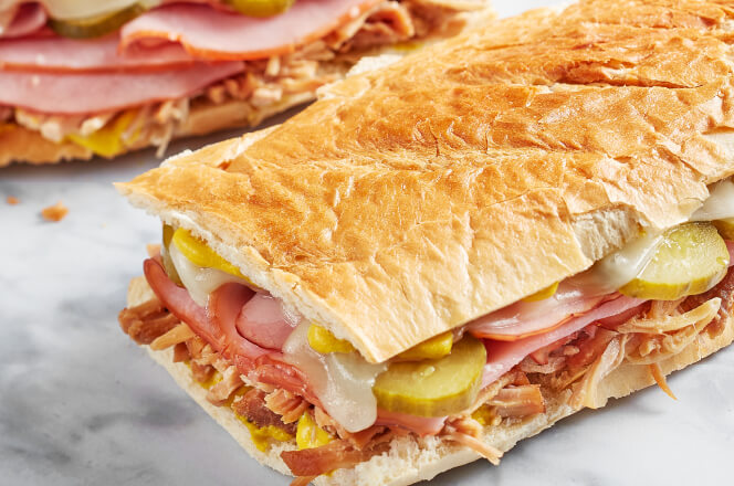 A foot-long Cuban sub filled with ham, pulled pork, Swiss cheese, pickles, and mustard.