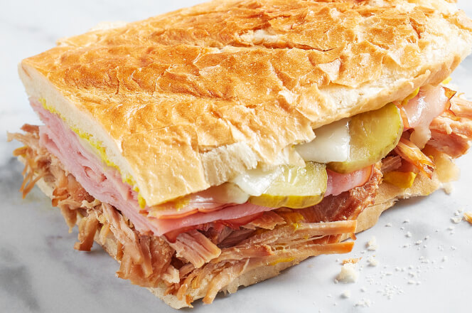 A Cuban sandwich with layers of ham, roasted pork, Swiss cheese, pickles, and mustard on pressed bread.