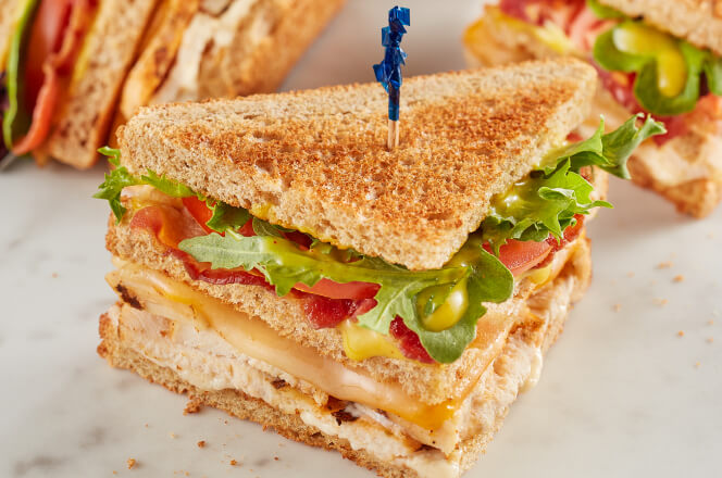 A Grilled Chicken Club sandwich with grilled chicken, bacon, cheddar, lettuce, tomato, and honey mustard on toasted bread.