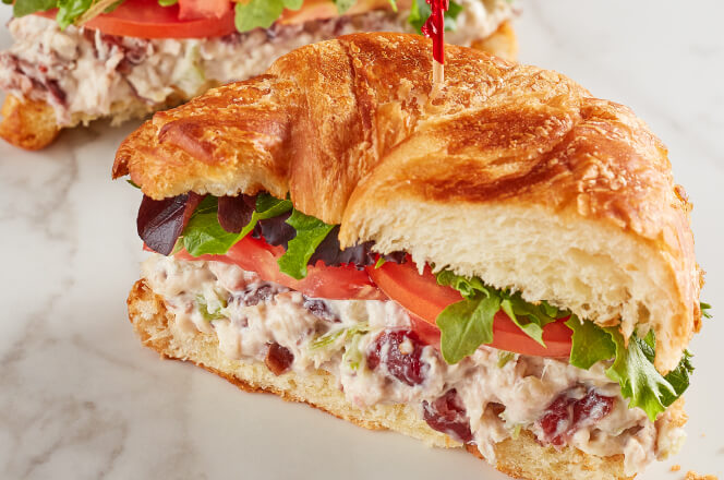 A Harvest Chicken Salad sandwich featuring a creamy chicken salad with cranberries and pecans on a croissant.