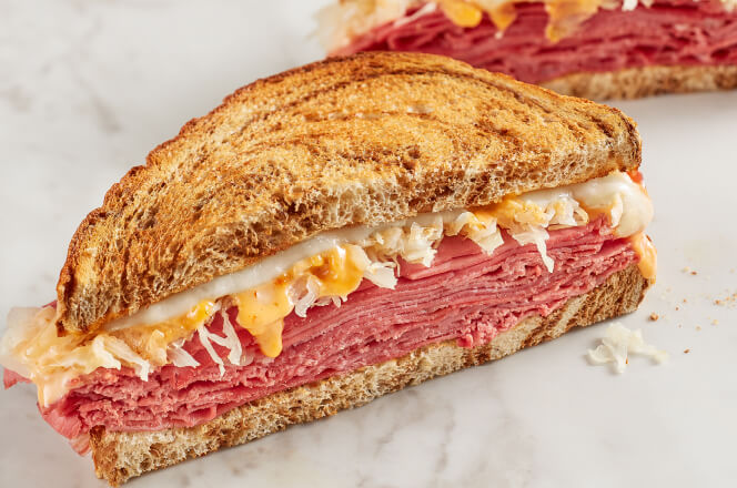 A Reuben sandwich with corned beef, Swiss cheese, sauerkraut, and Thousand Island dressing on toasted rye bread.