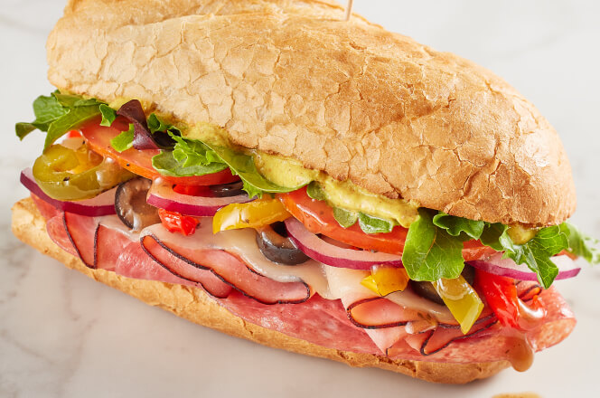 An Italian sub with layers of ham, salami, pepperoni, provolone cheese, lettuce, tomato, red onions, and vinaigrette on toasted bread.