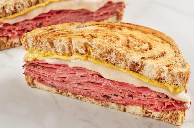 A pastrami and corned beef sandwich with Swiss cheese, and spicy mustard on marbled rye bread.