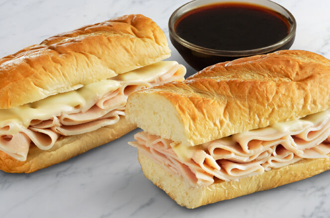 A 12-inch turkey dip sub with layers of tender, sliced turkey and melted Swiss cheese on a toasted baguette, served with a side of savory au jus for dipping