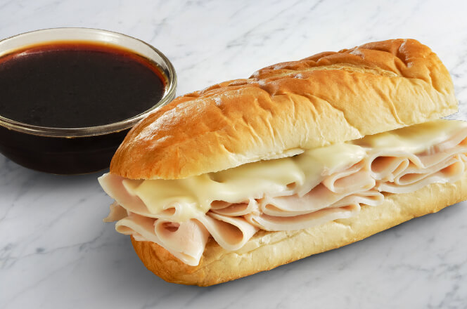 A 6-inch turkey dip sub-marine sandwich on a toasted baguette, filled with sliced turkey and melted Swiss cheese, served with a side of au jus for dipping.
