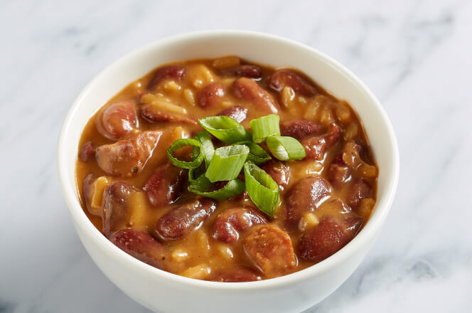 A bowl of Cajun red beans and rice, featuring seasoned red beans, andouille sausage, and white rice, garnished with herbs.