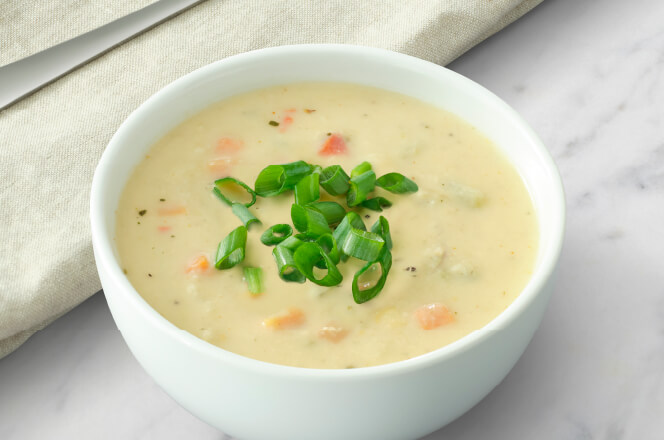 A cup of Kickin’ Crab Chowder, a creamy soup with chunks of crab and vegetables, garnished with herbs.