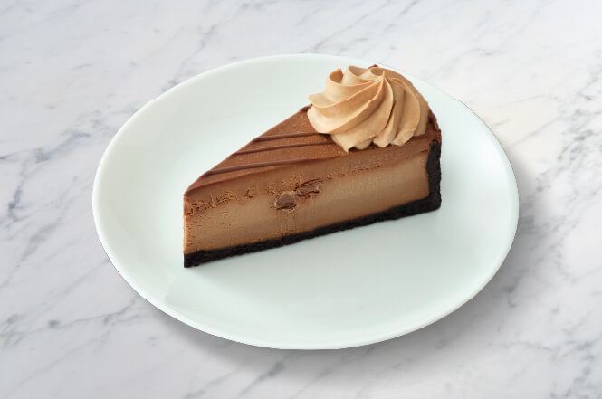 A decadent slice of Godiva chocolate cheesecake with a chocolate crust and drizzle.